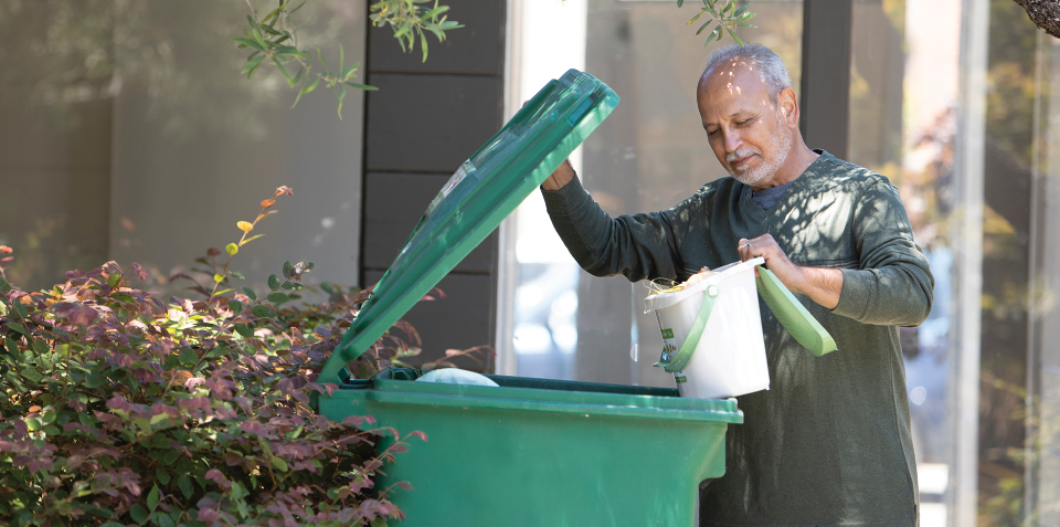 A man pours in the contents from a smaller compost bucket into his green compost cart