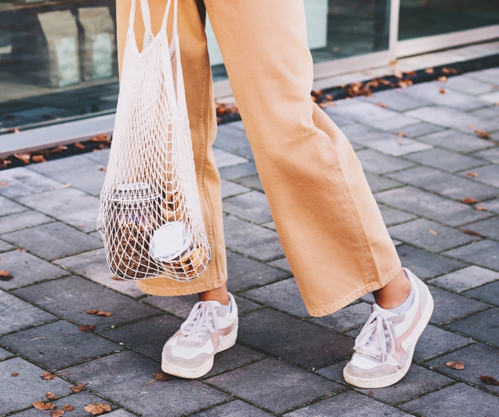 A person holding a mesh reusable shopping bag with jars of food inside of it