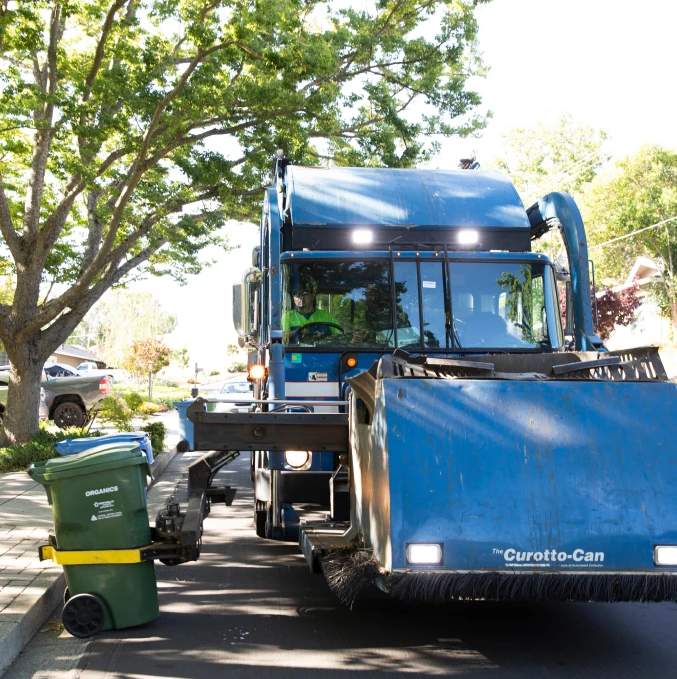 A Republic Services truck lifts a green organics cart on a residential street